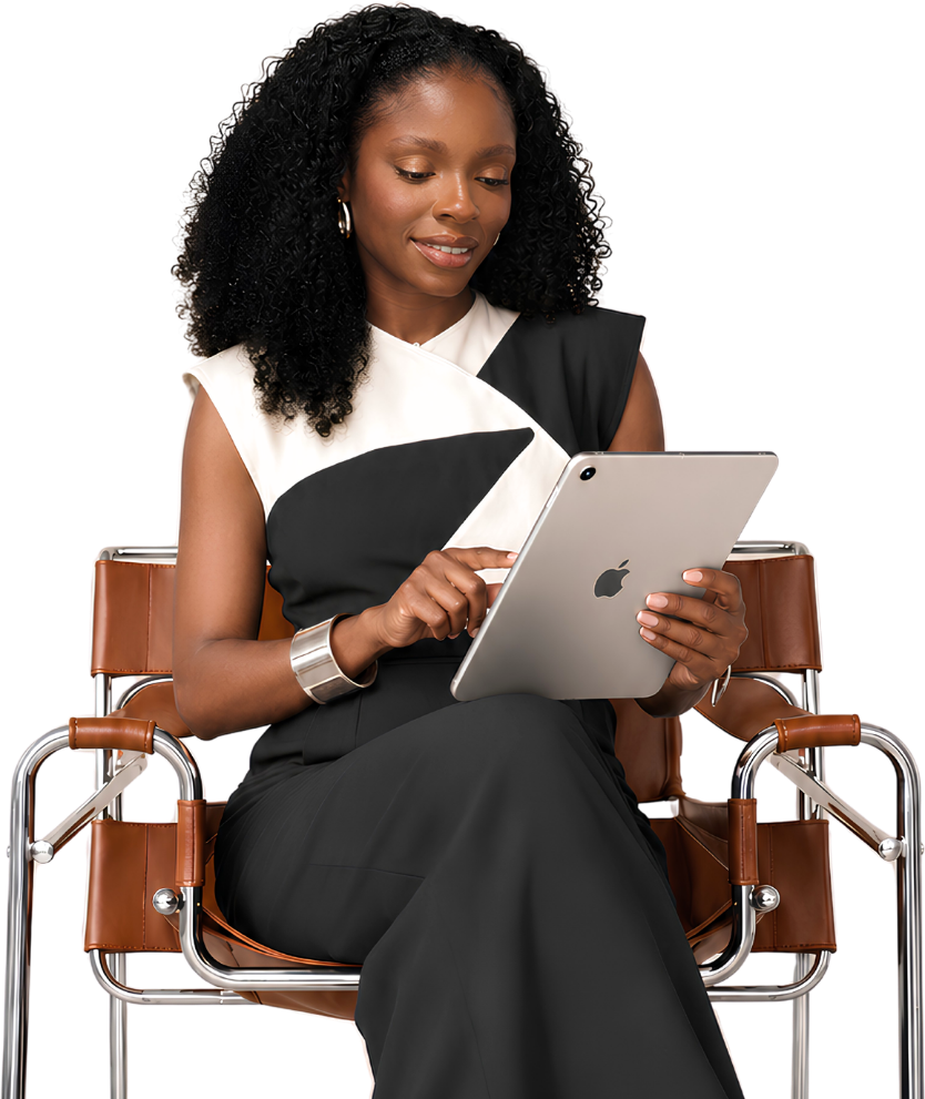 Editorial portrait: a woman with curly hair seated in a chrome-and-leather chair, working on an iPad